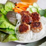 Close up side view of Bún chả in a bowl with rice noodles and vegetables.