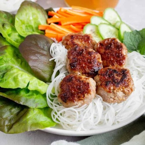 Close up side view of Bún chả in a bowl with rice noodles and vegetables.