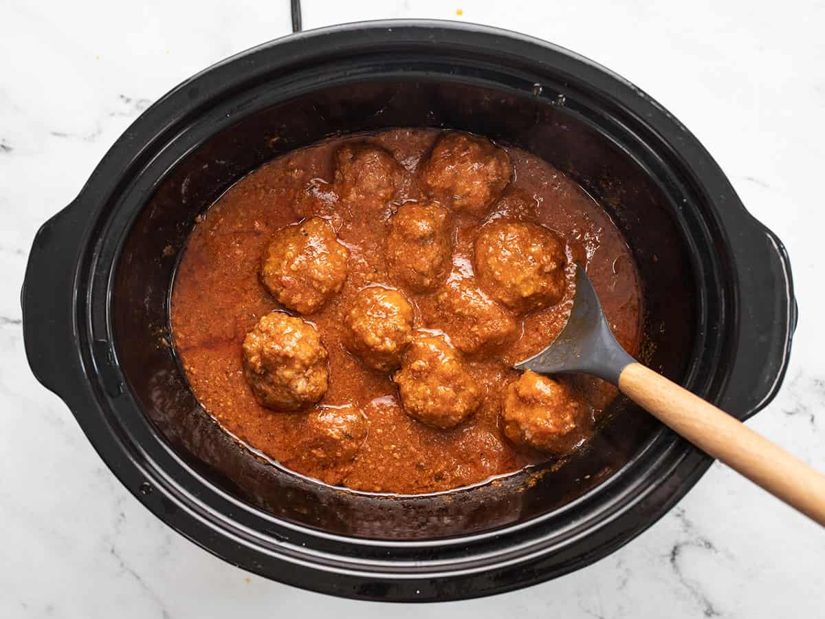 Finished slow cooker meatballs in the slow cooker with a spoon.