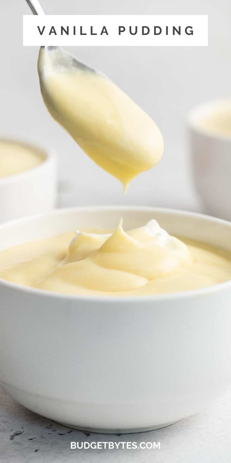Side shot of vanilla pudding in a white bowl with a spoon coming out of it.
