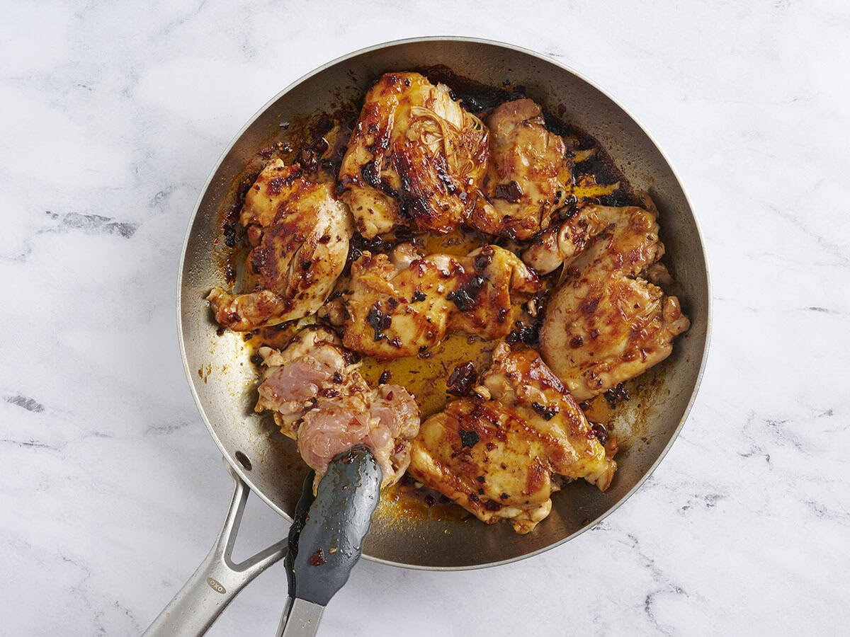 Kitchen tongs flipping chipotle honey chicken in a skillet.