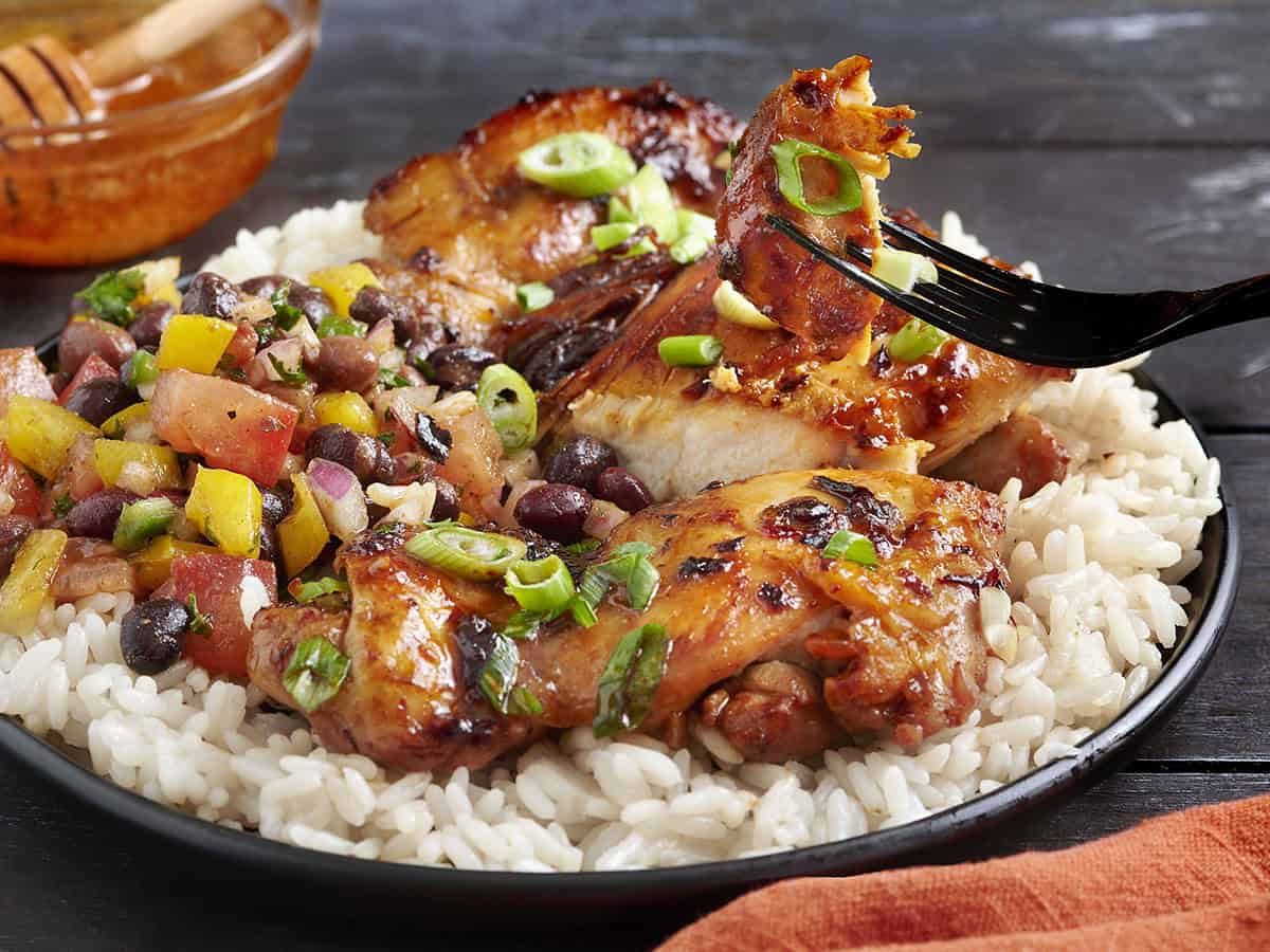 Side view of chipotle honey chicken on a plate with cowboy caviar and white rice.
