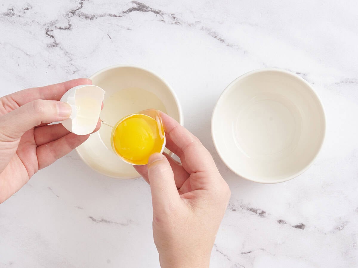 Hands separating egg whites from an egg yolk.