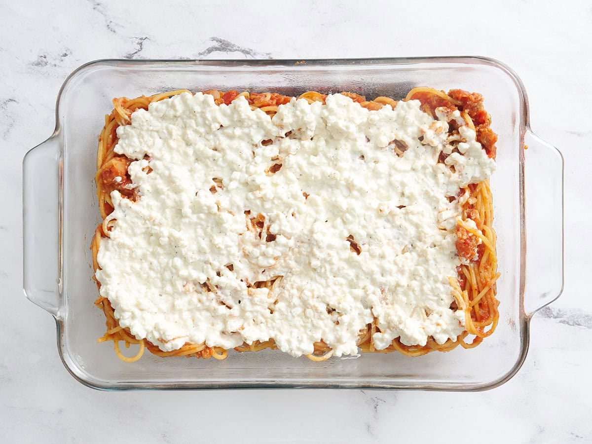 Spaghetti and meat sauce in a baking dish with a cottage cheese and parmesan mix added on top.