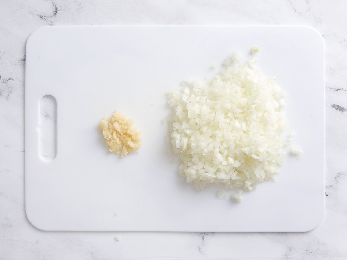 A diced onion and minced garlic on a cutting board.