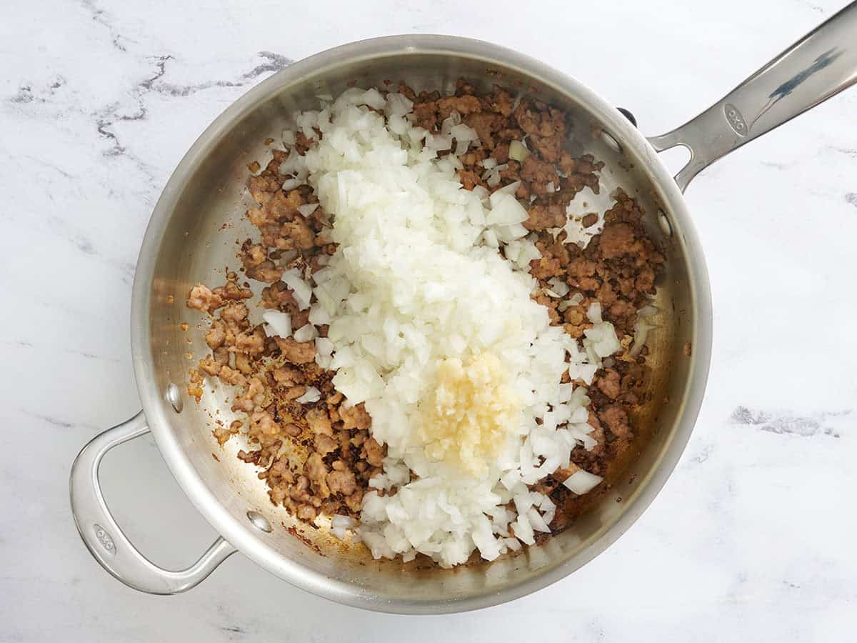 Minced garlic and diced onion added to browned sausage in a skillet.
