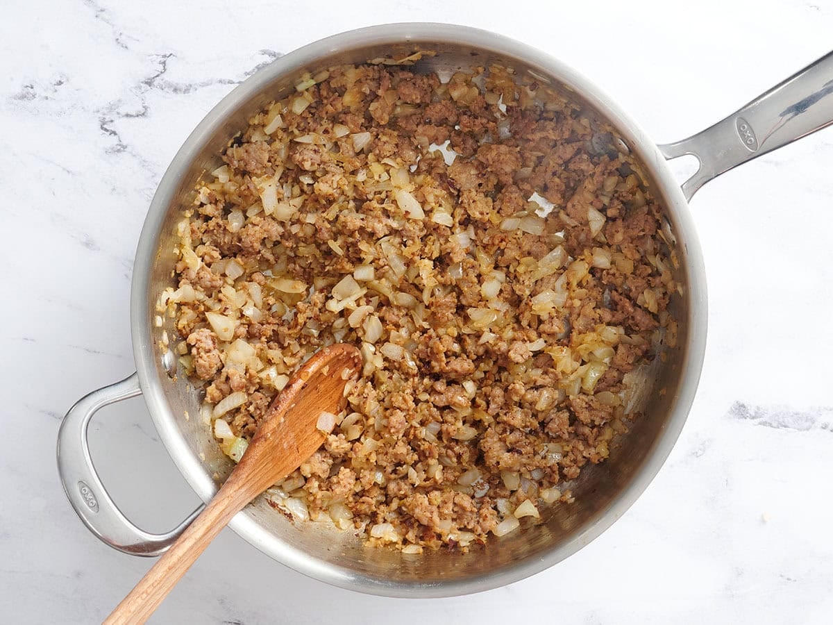Softened onions and cooked sausage in a skillet.
