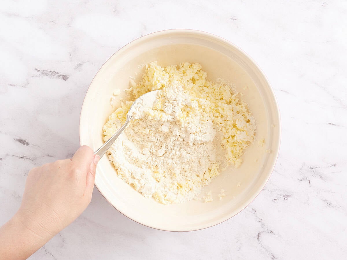 Flour and grated butter being combined in a mixing bowl.