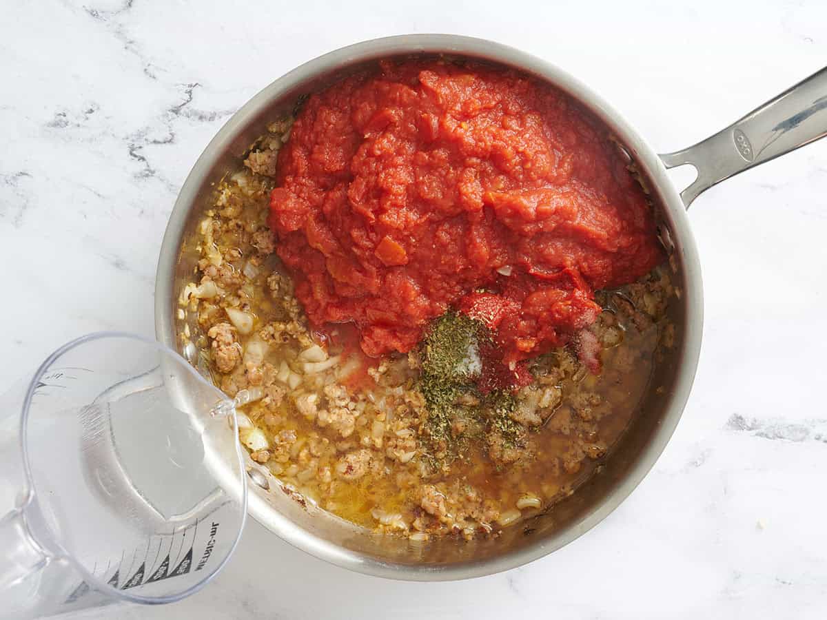 Seasonings and tomato paste added to cooked sausage in a skillet.
