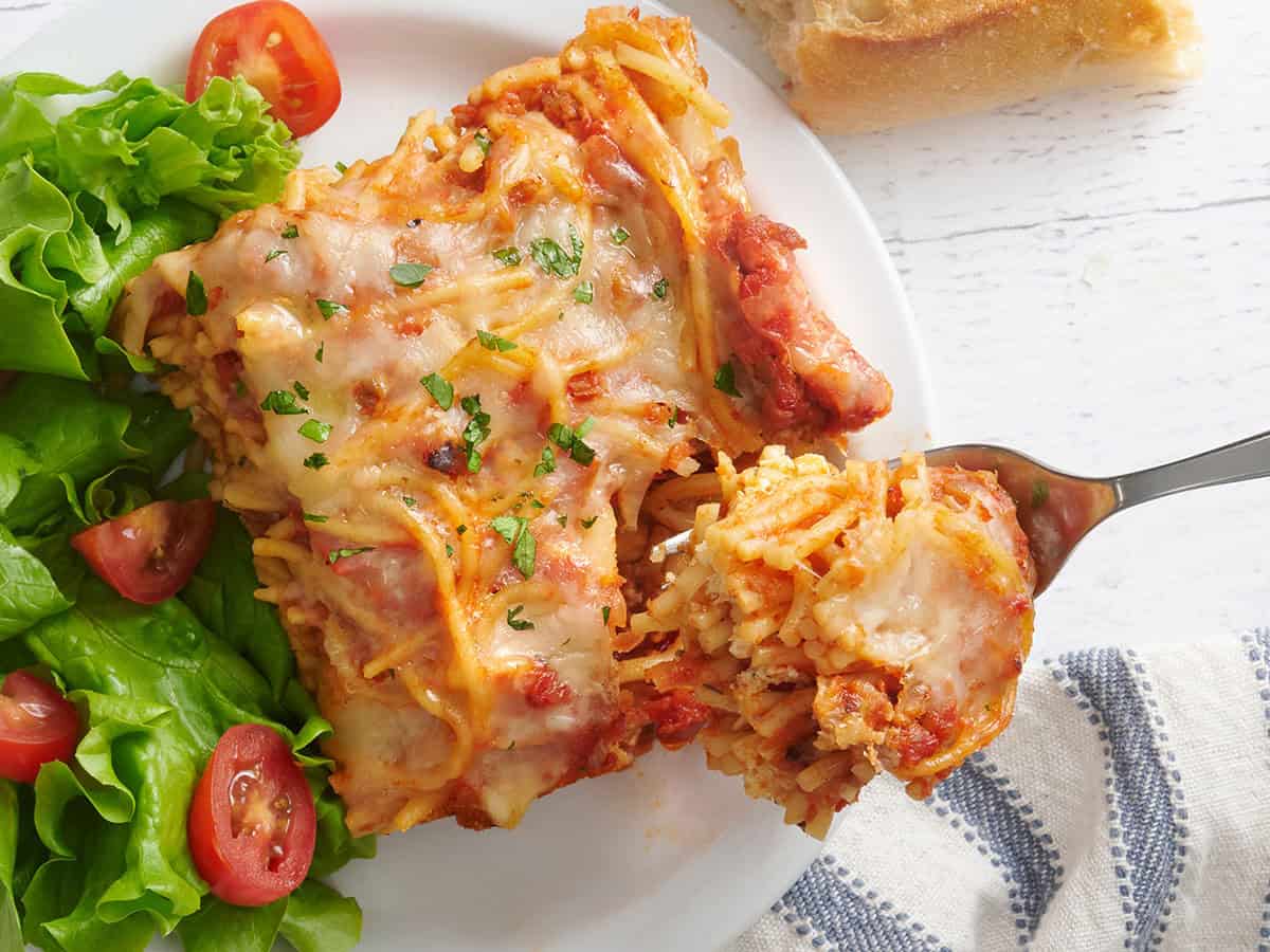 A piece of baked spaghetti on a plate with a fork taking some.