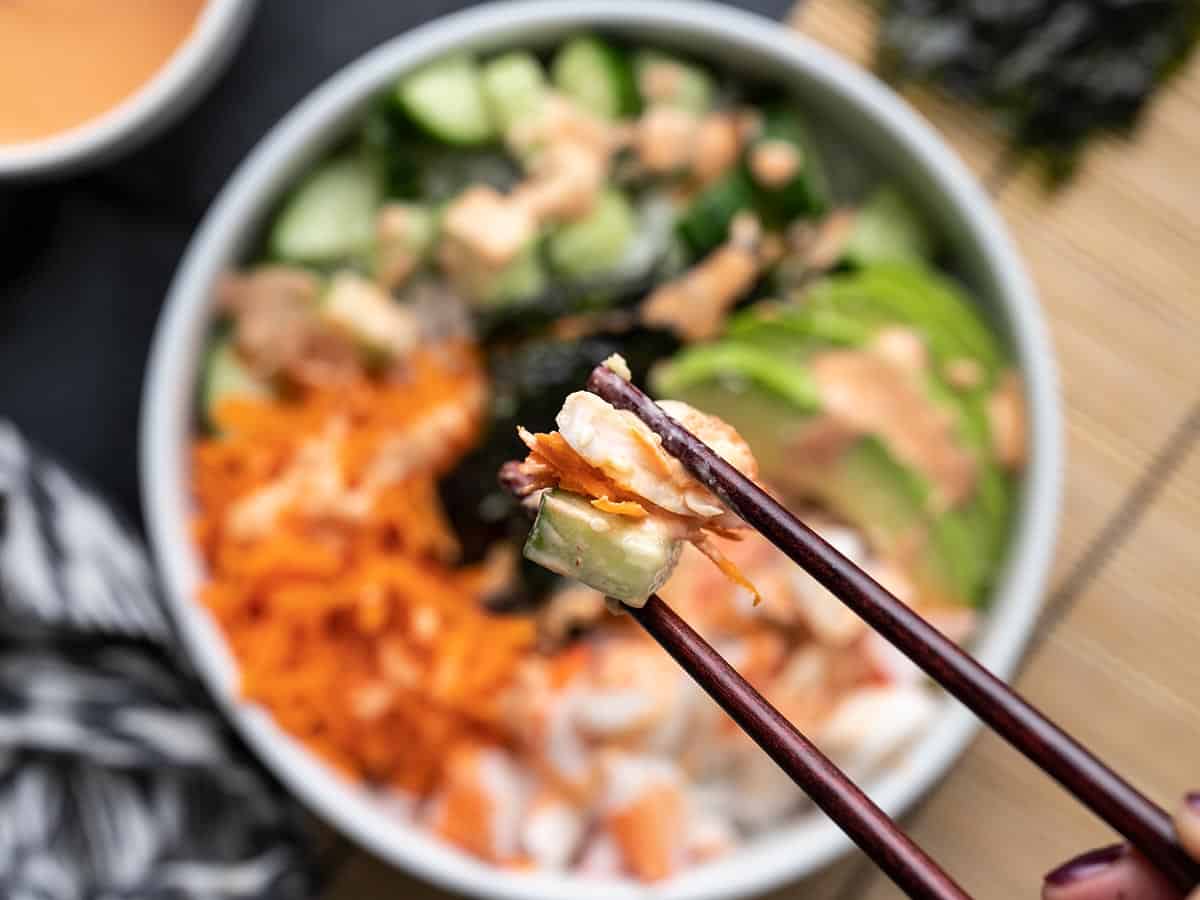 Homemade Sushi Bowls are a fast, easy, and inexpensive alternative to your favorite sushi bar. Get your sushi fix without spending a fortune. BudgetBytes.com Close up of a bite of sushi bowl being held by chopsticks.