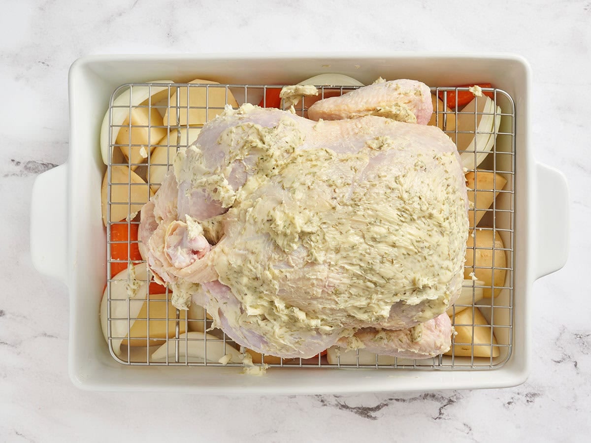 A trussed chicken over vegetables in a baking dish.