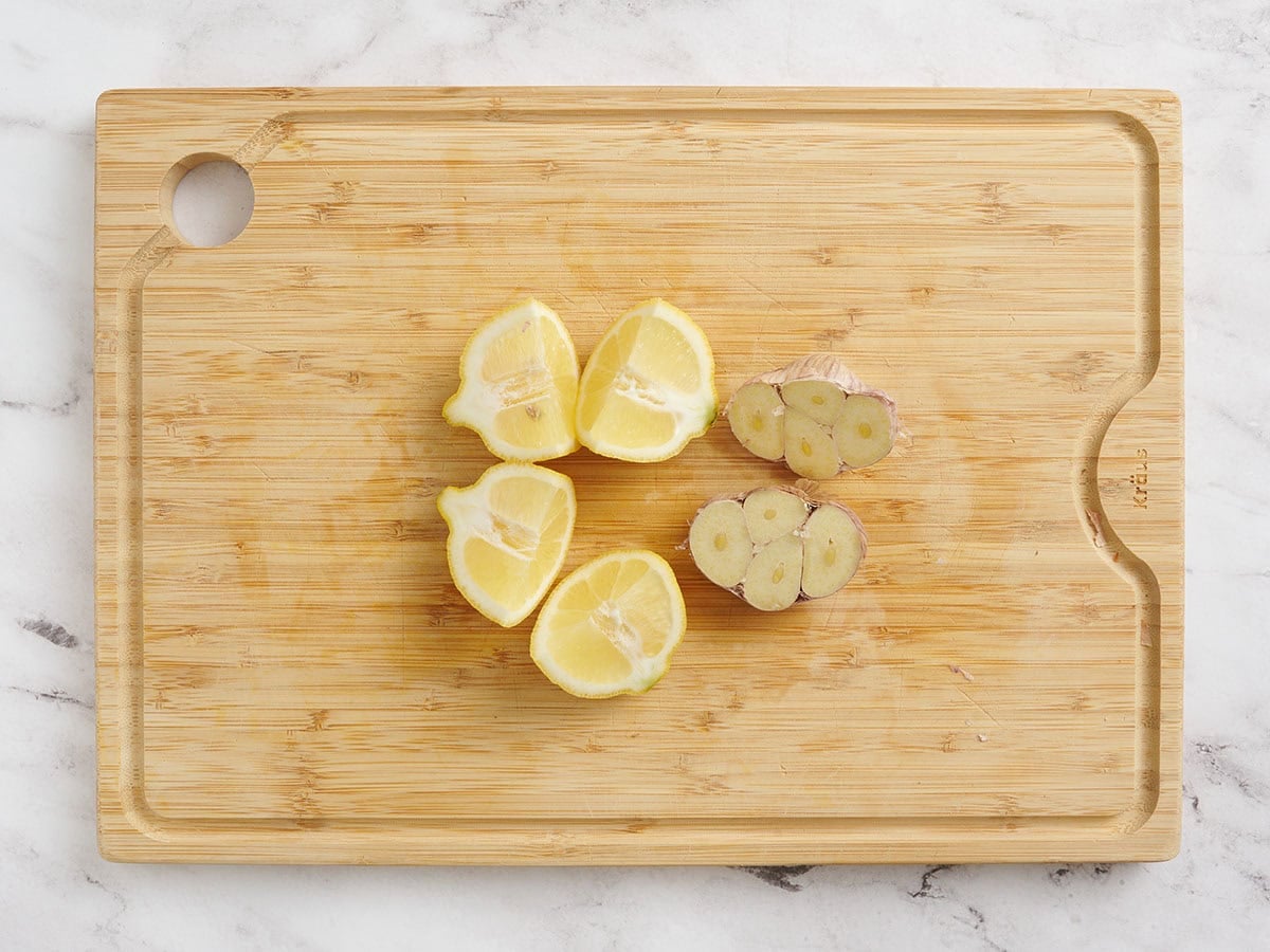 Lemon and a head of garlic sliced in half on a wooden cutting board.