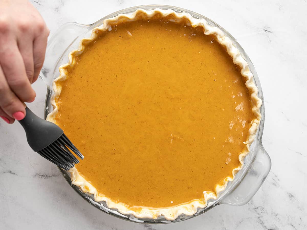 Heavy cream being brushed onto the crust of a pumpkin pie.