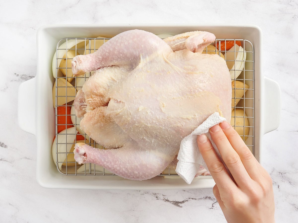 A whole chicken being wiped with a paper towel.