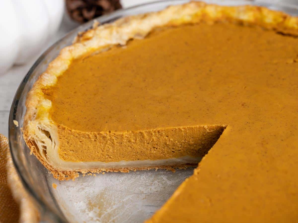 Side view of a pumpkin pie with a slice taken out.