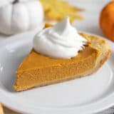 Side shot of a slice of pumpkin pie with a dollop of whipped cream on top of it.