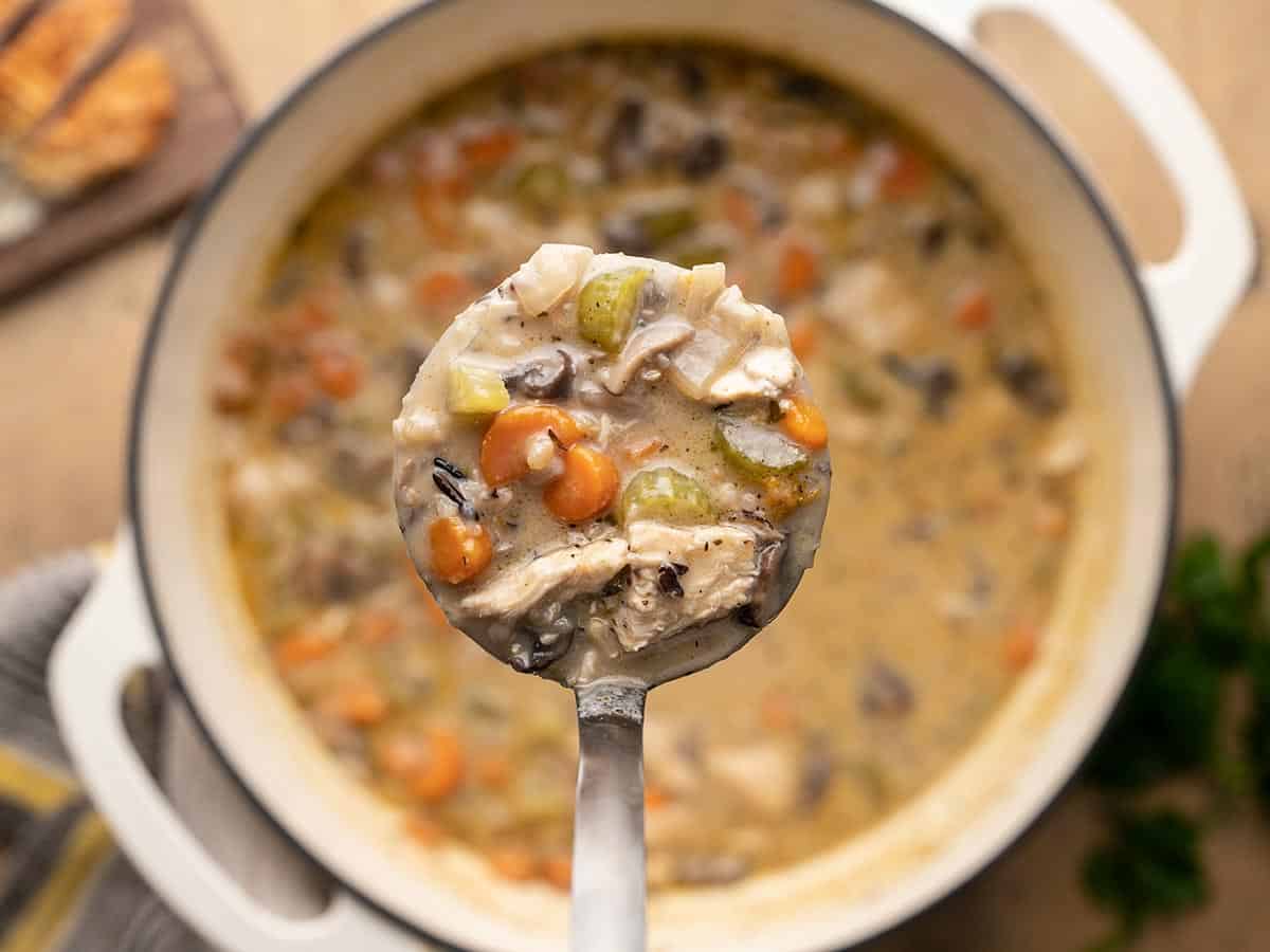 Close up of a ladle full of turkey and wild rice soup over the pot.