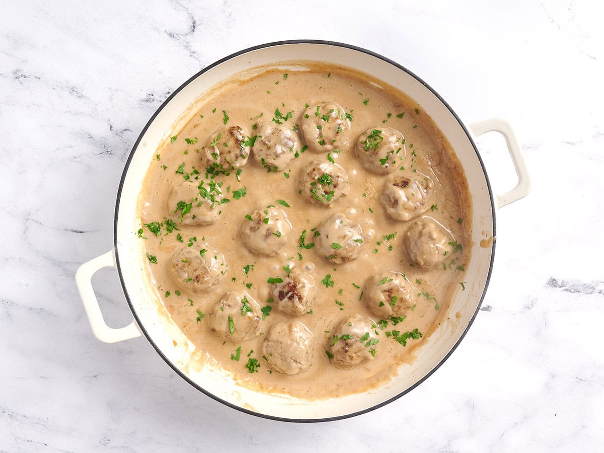 Homemade Swedish meatballs in a pot garnished with fresh herbs.