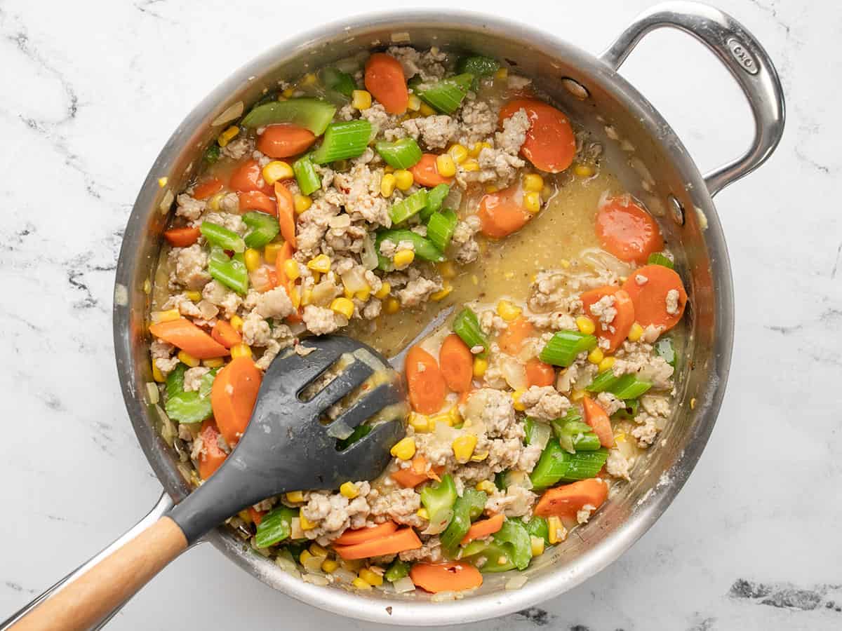Overhead view of the finished chicken and biscuit casserole base with a serving spoon to show that the broth reduced but is still slightly soupy.