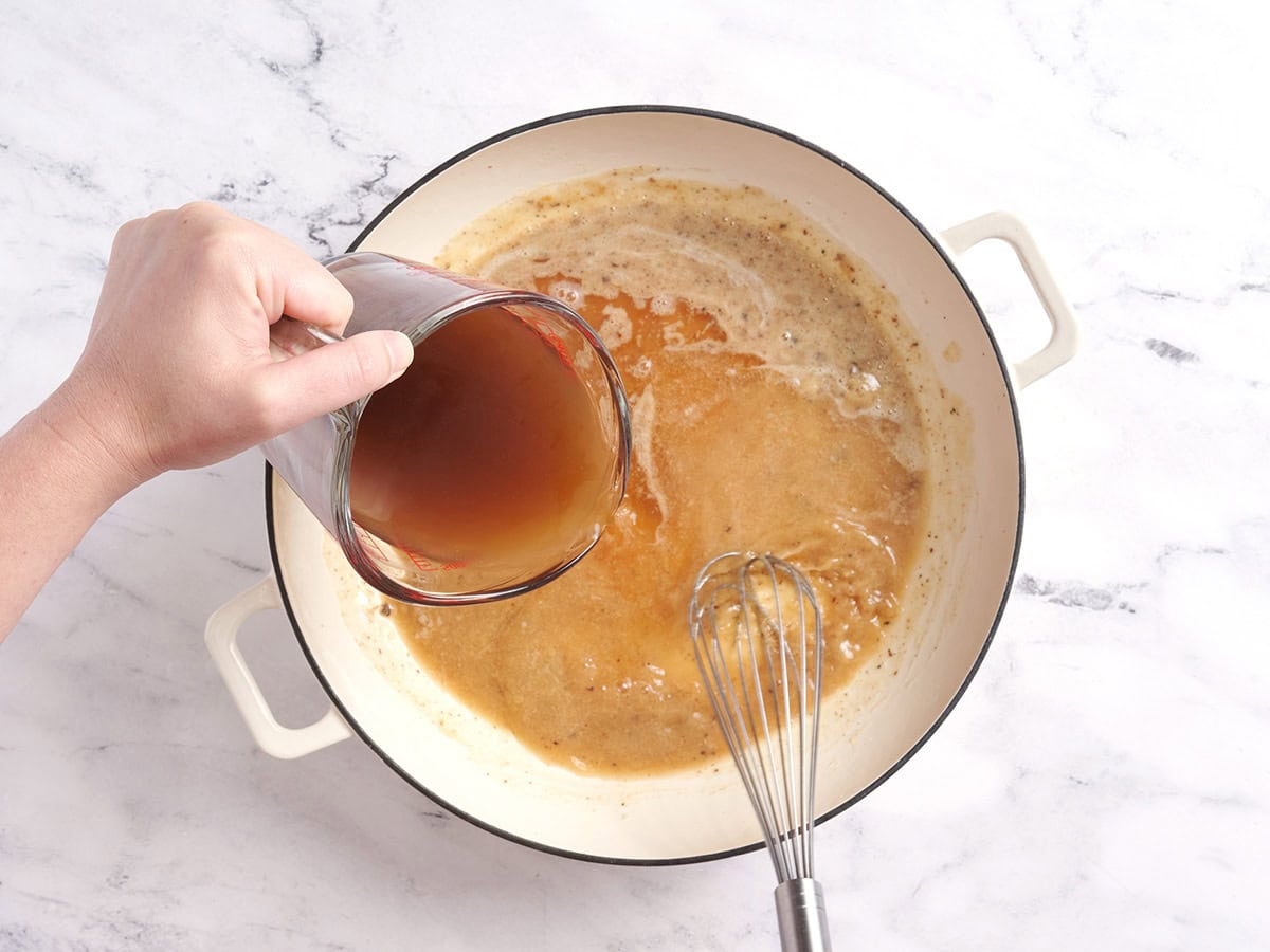 Beef broth added to a roux in a pot.