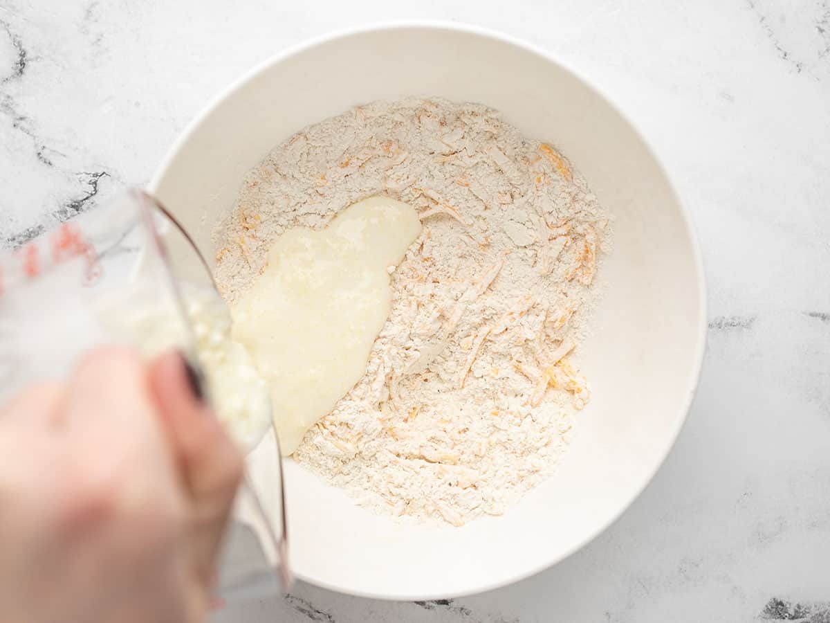 Cook pours mixed buttermilk and melted butter into a while bowl with dry ingredients to make cheddar biscuits.