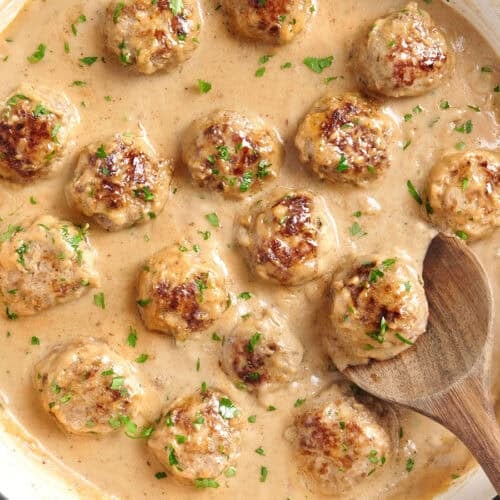 Overhead view of swedish meatballs in a skillet with a wooden spoon.
