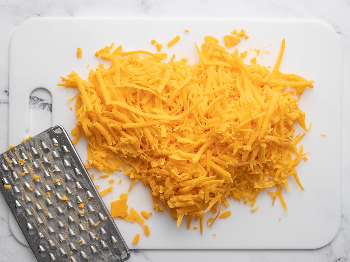 Shredded cheddar cheese on a cutting board with the cheese grater.