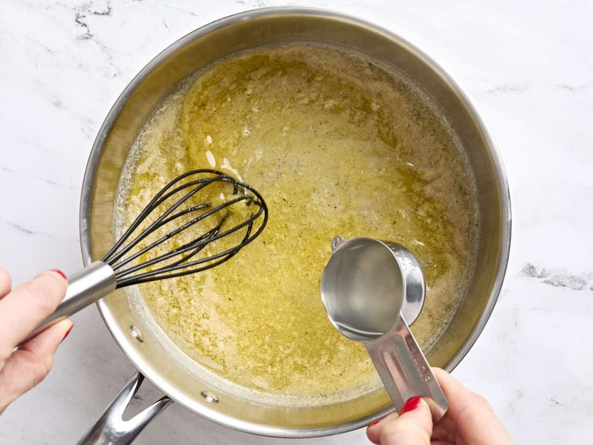 Reserved pasta water being whisked into melted butter in a skillet.