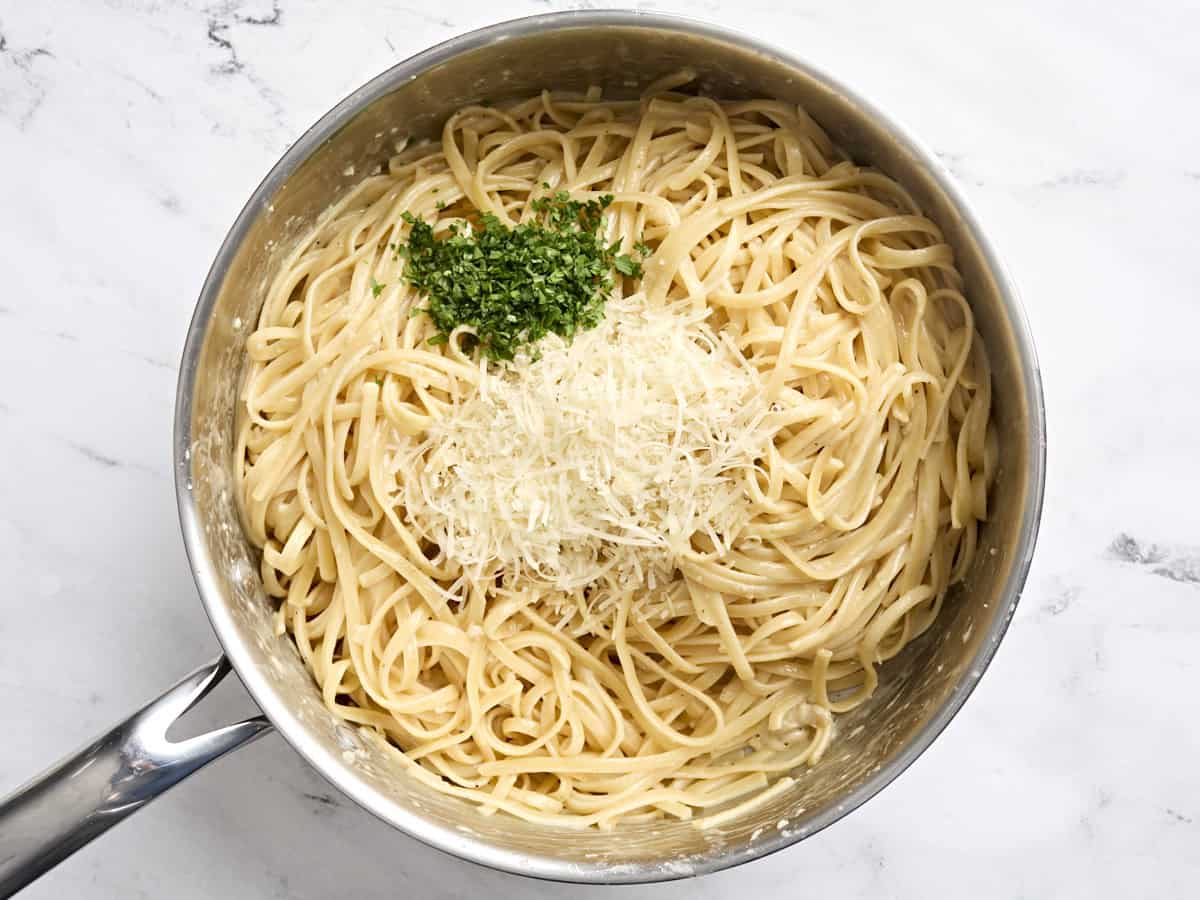 Parmesan cheese and fresh parsley added to a skillet of Fettuccine alfredo.