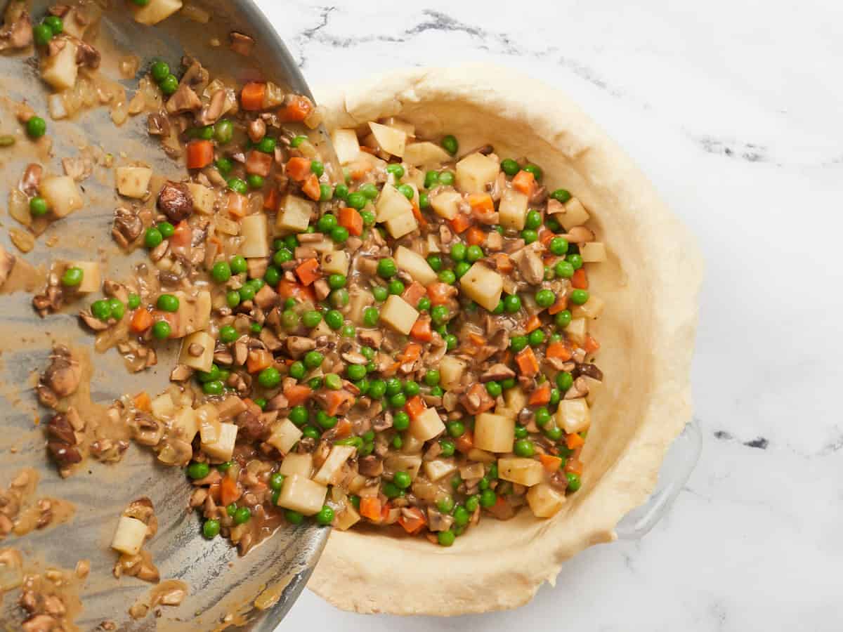 The filling for a vegetarian pot pie being poured into a pie dish lined with a homemade pie crust.