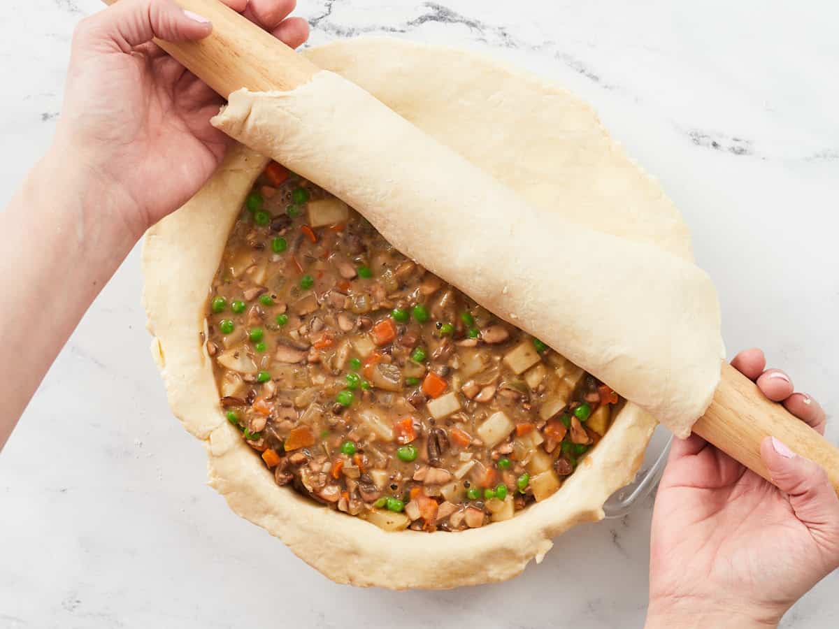 Hands using a rolling pin to roll out the top crust over a homemade veggie pot pie.