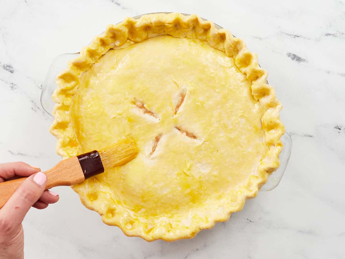 A brush topping a vegetarian pot pie with egg yolk before baking.