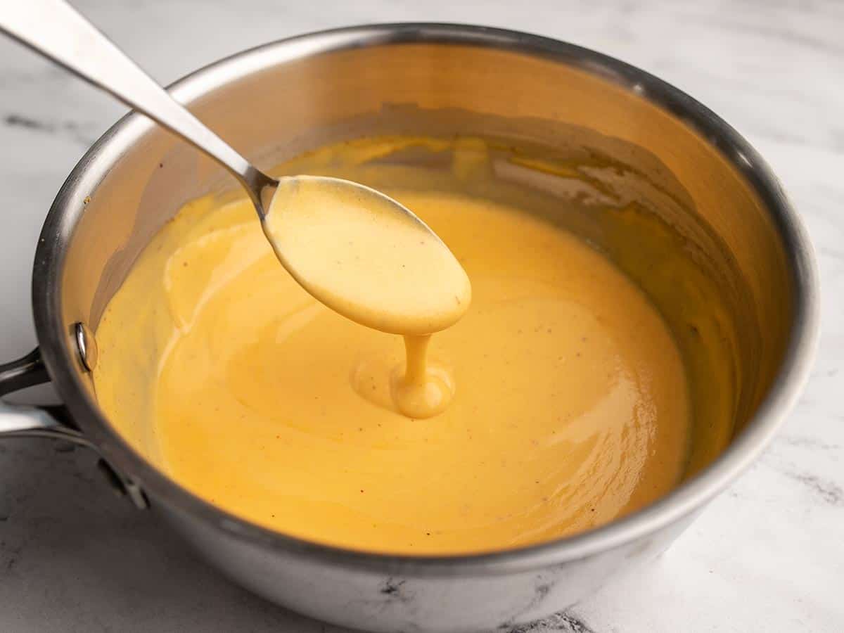 Nacho cheese running off a spoon into a saucepot.