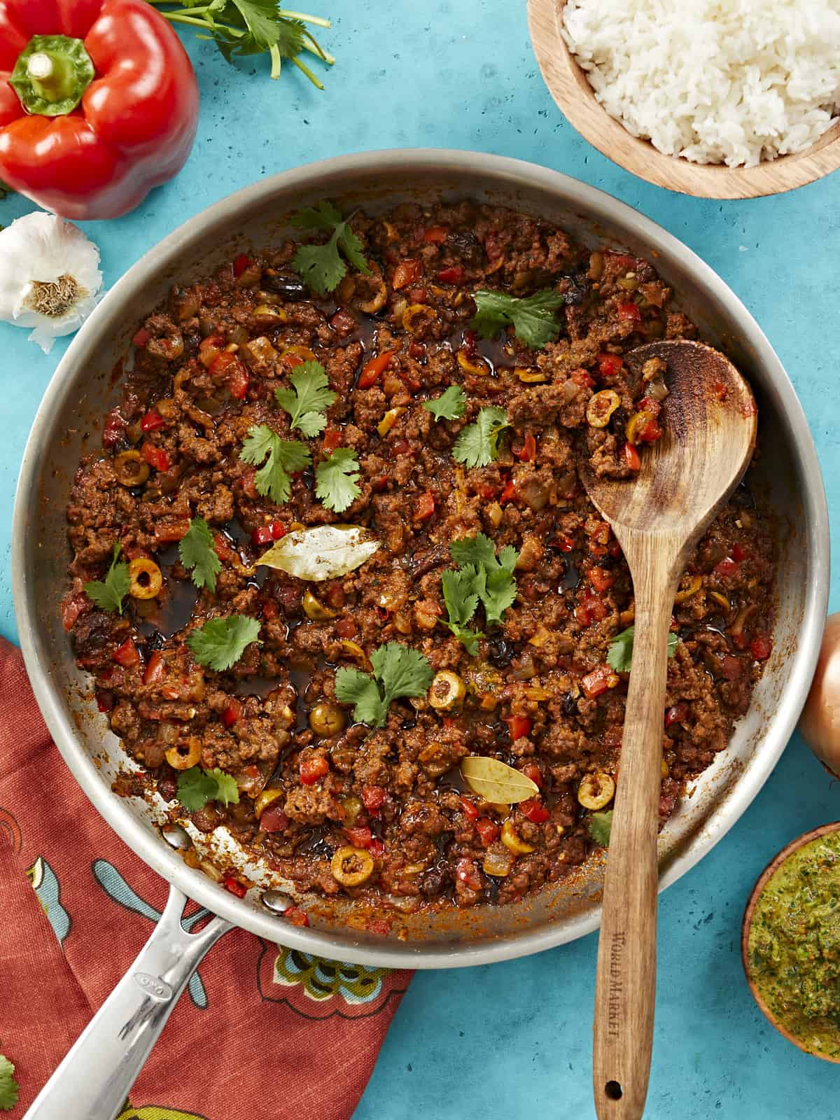 Overhead view of picadillo in a skillet with a wooden spoon.