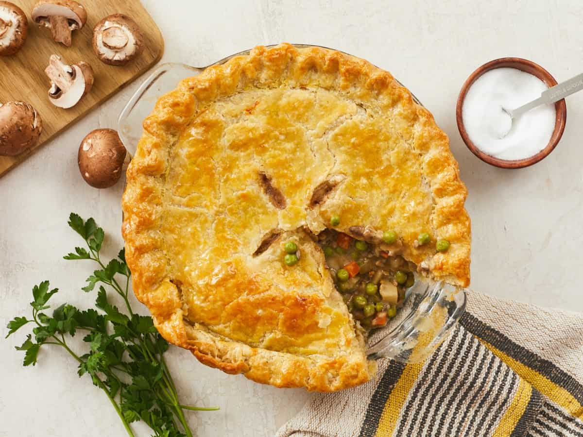 A homemade vegetable pot pie in a pie dish with a slice missing.