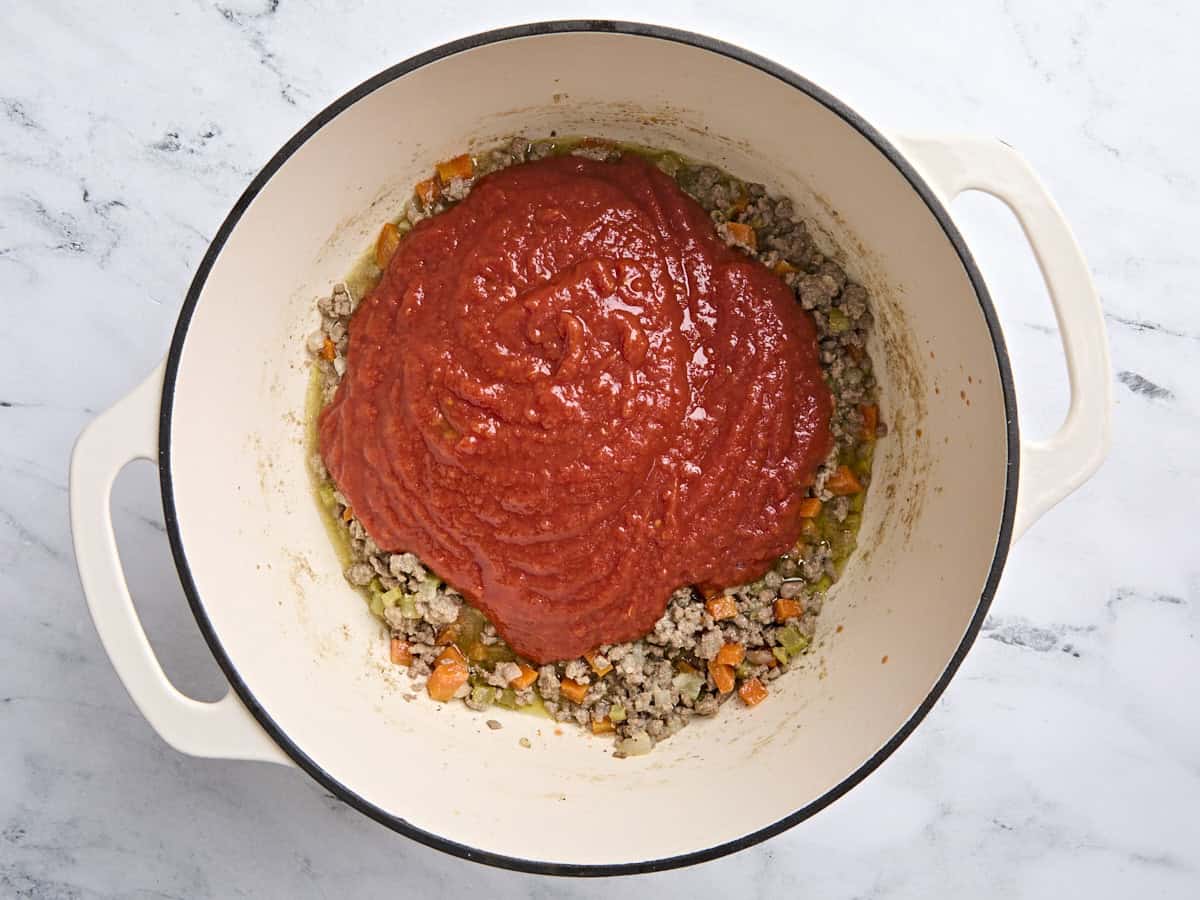 Crushed tomatoes added to a Dutch oven with vegetables and browned ground beef to make a bolognese sauce.