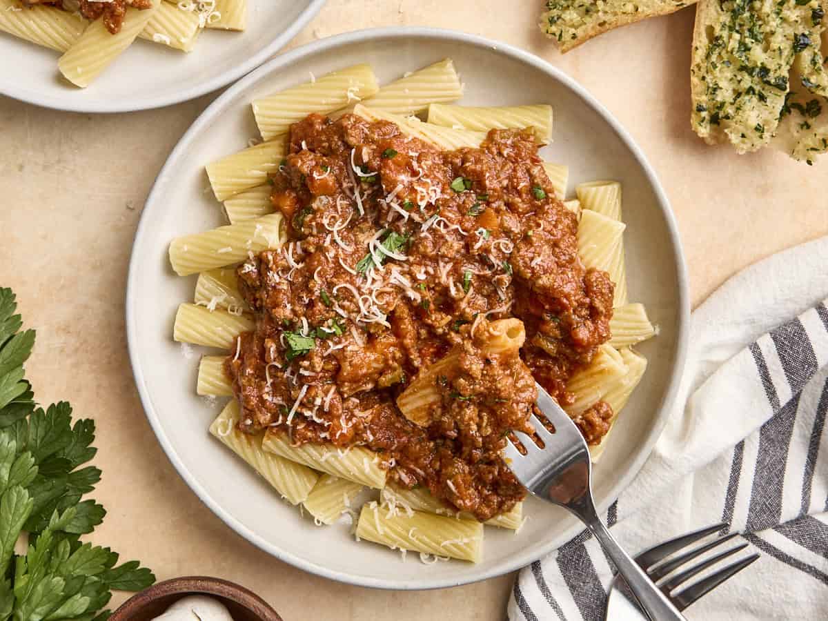 Homemade Bolognese sauce on a bed on pasta on a plate, with a fork taking some.
