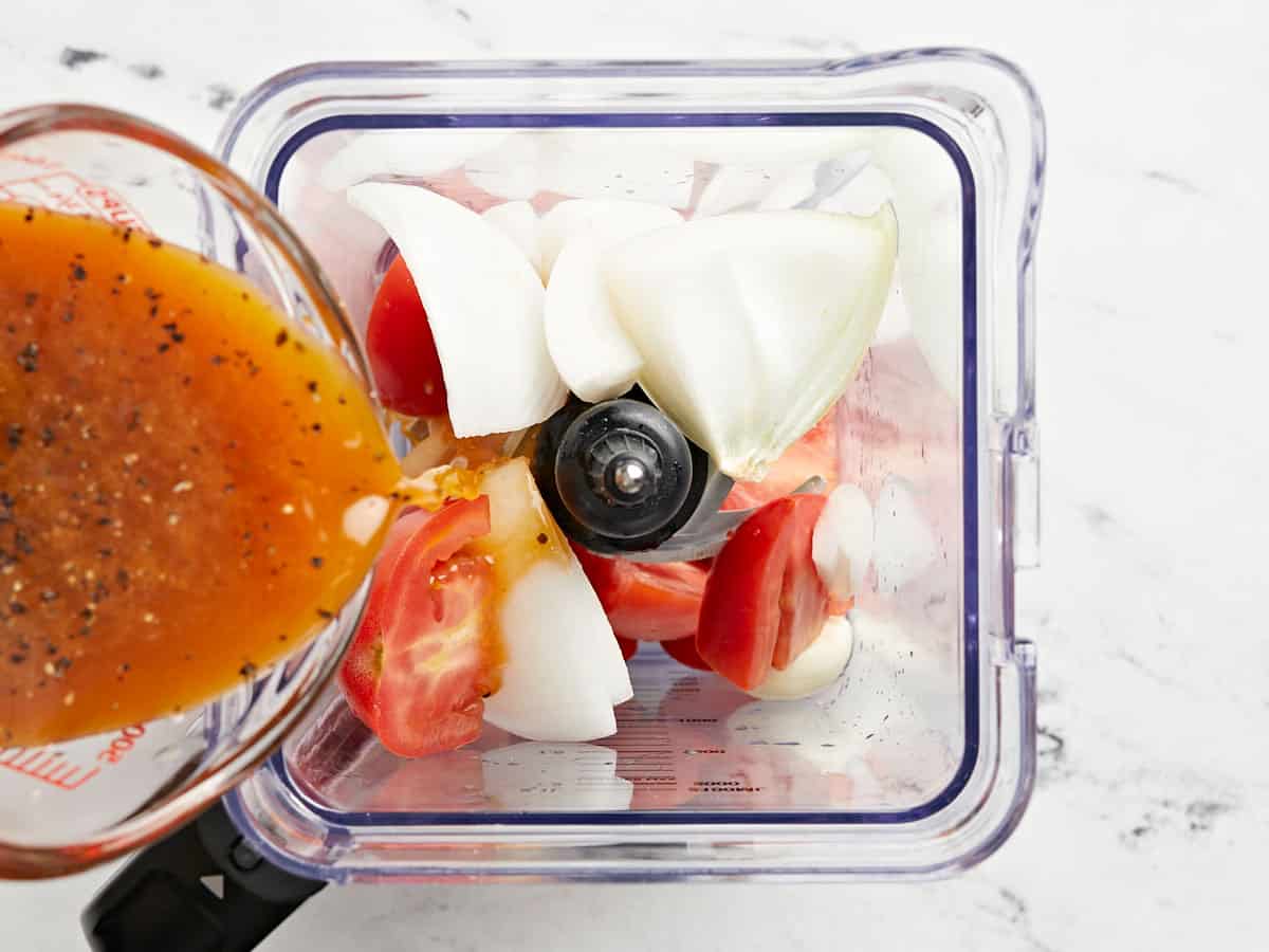 Broth and herbs being poured into a blender with vegetables.