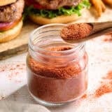 Side view of homemade burger seasoning in a jar with a spoon.