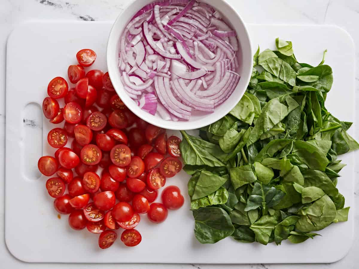 Sliced onions in a bowl, halved grape tomatoes, and chopped spinach.