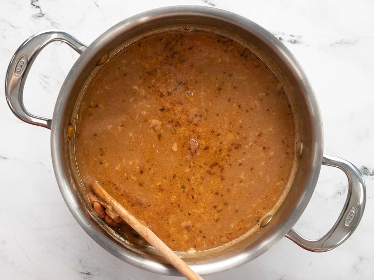Beans being smashed on the side of the pot with a wooden spoon.