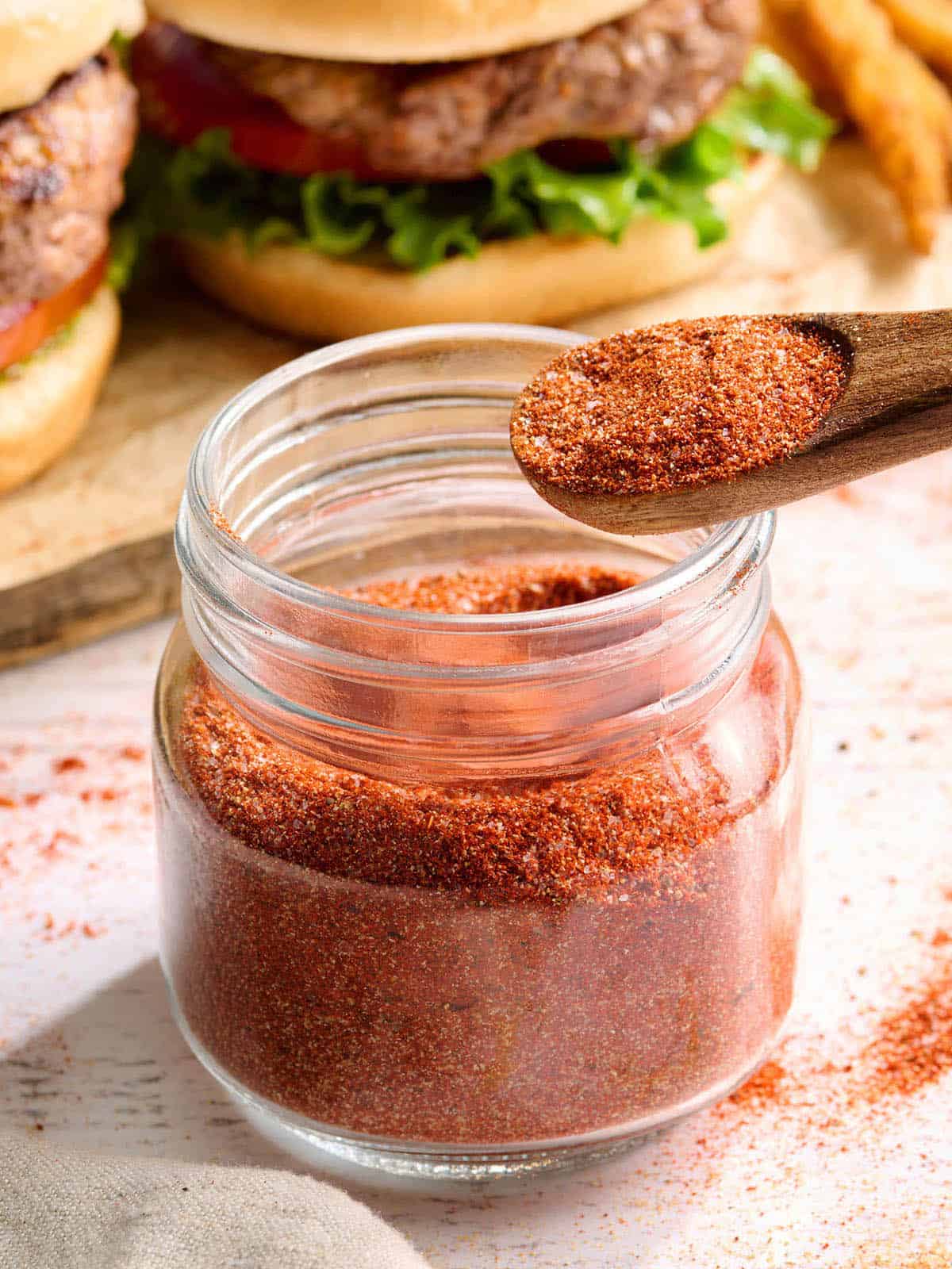 Side view of homemade burger seasoning in a jar with a spoon.