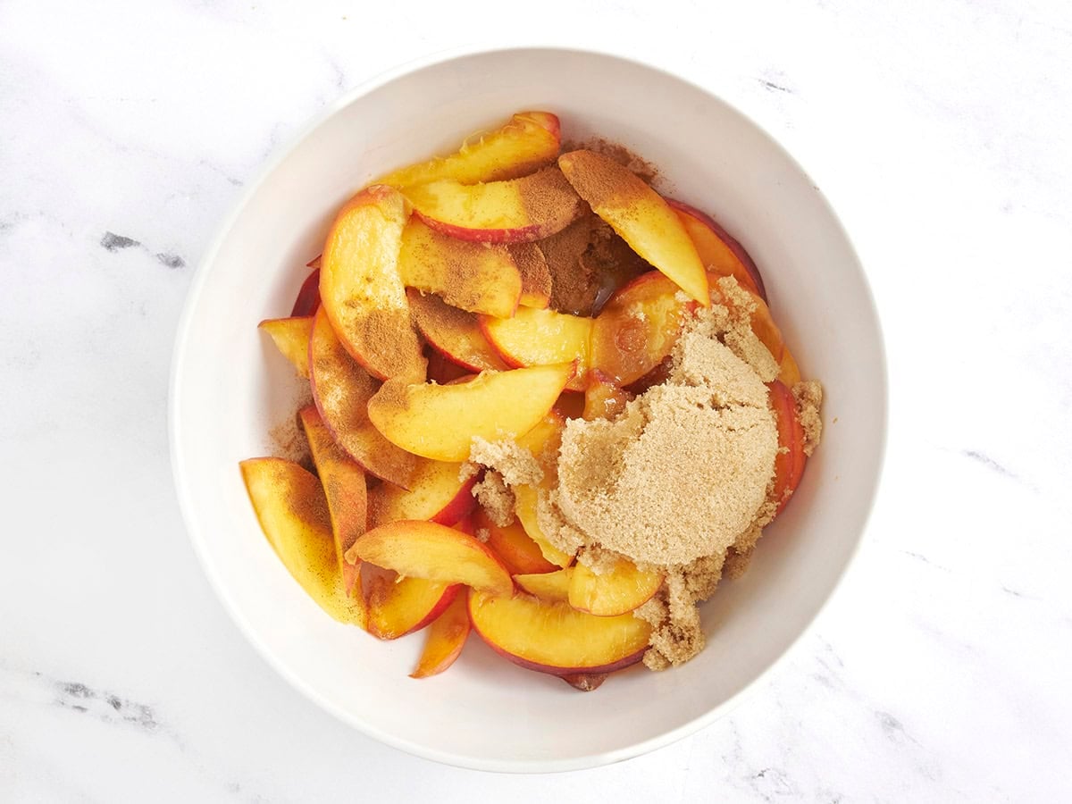 Brown sugar and cinnamon added to fresh peaches in a bowl.