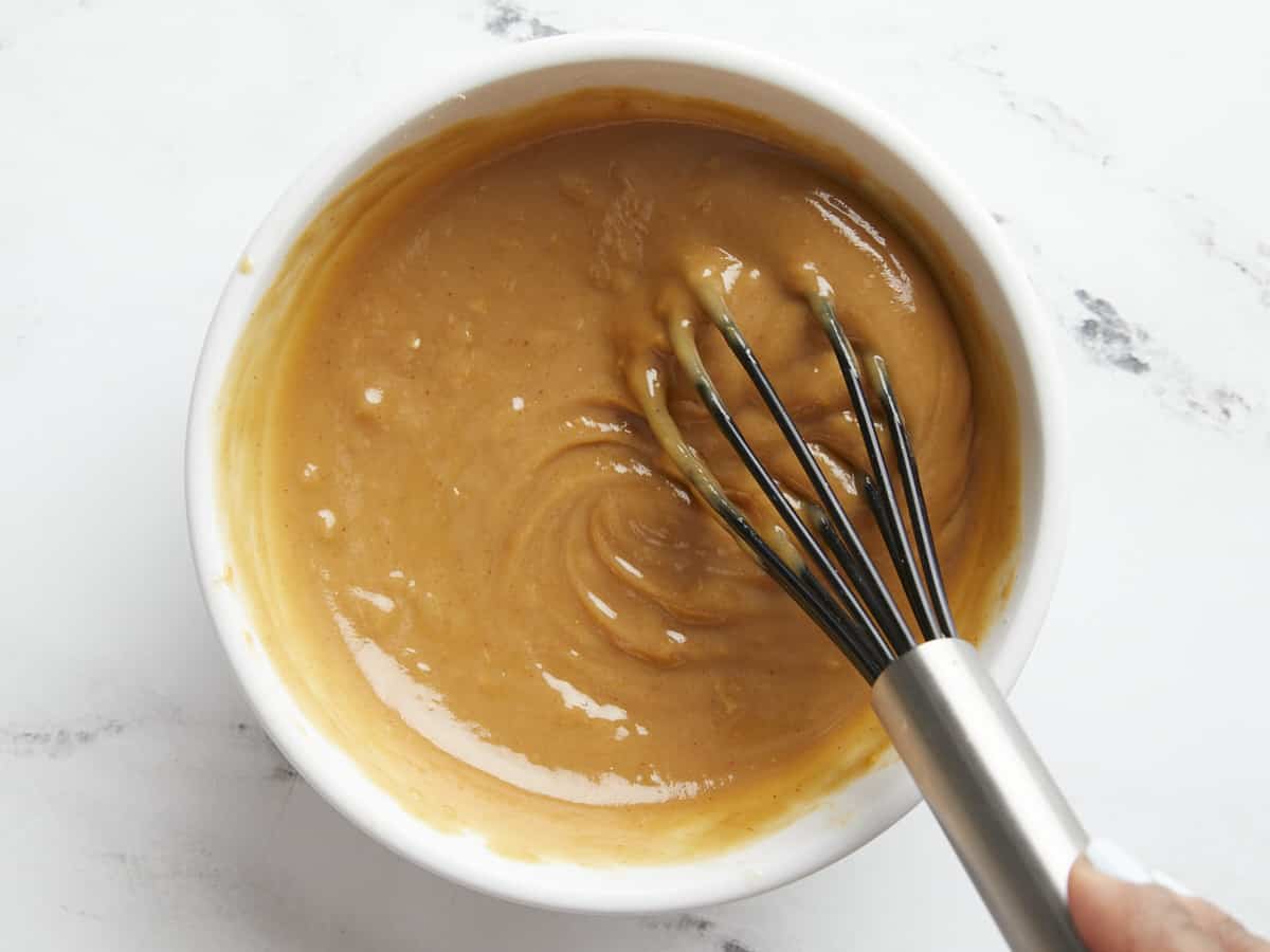 Overhead close up shot of peanut lime dressing in a white bowl with a whisk.
