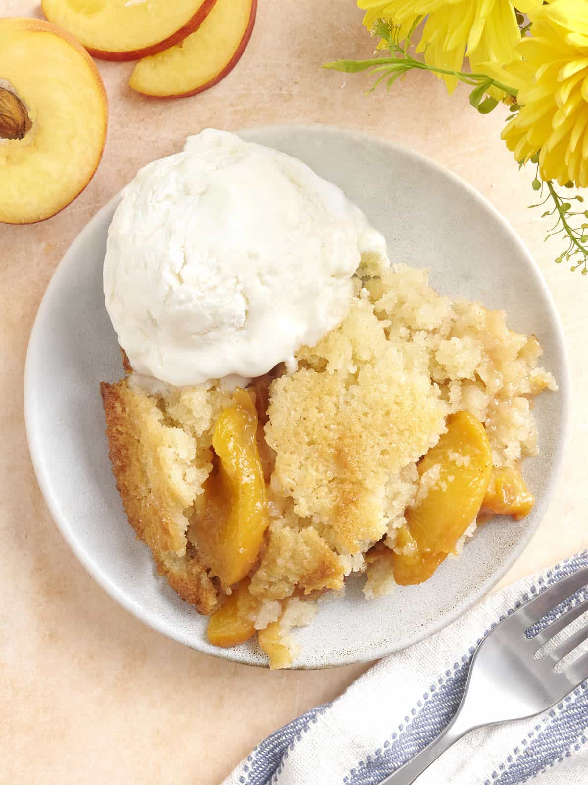 Overhead view of a bowl of homemade peach cobbler with a scoop of vanilla ice cream.