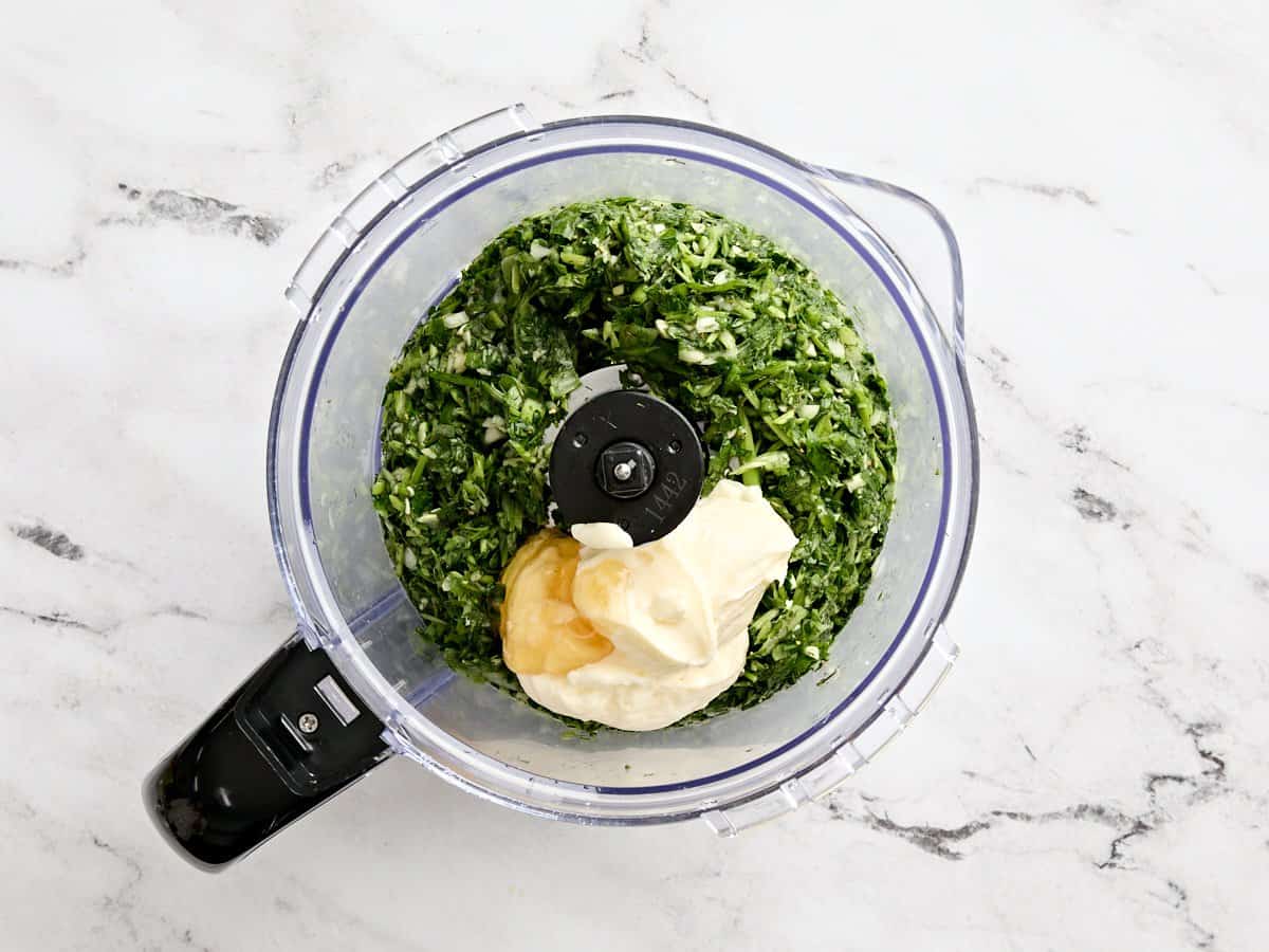 Mayonnaise, honey, and lemon juice added to a food processor with pulsed herbs.