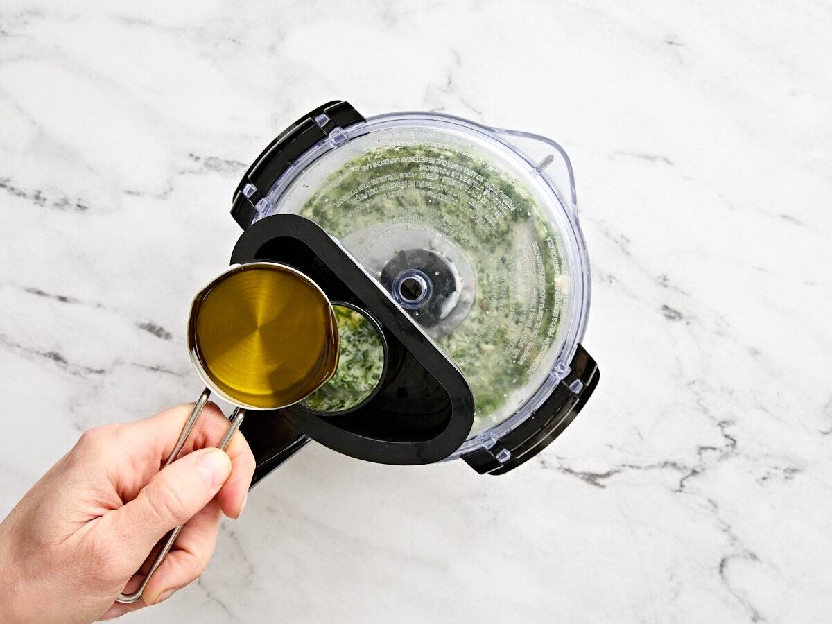 Oil being streamed into a food processor to make green goddess salad dressing.