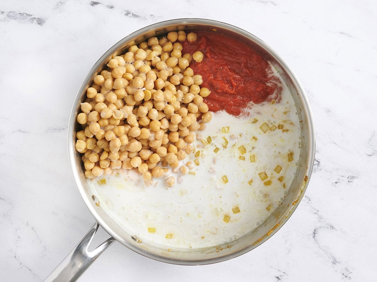 Coconut milk, chickpeas, and tomato in a skillet.