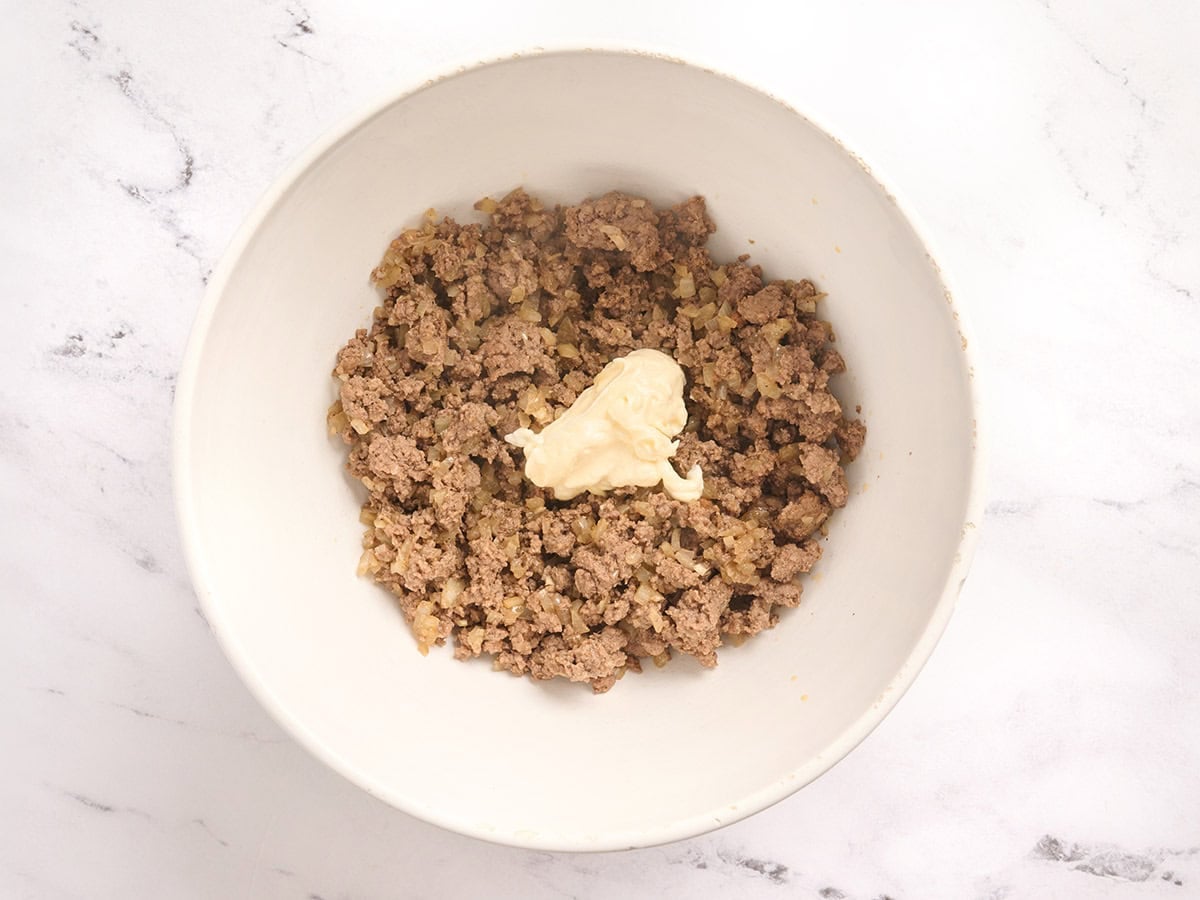 Mayo added to ground beef in a bowl.